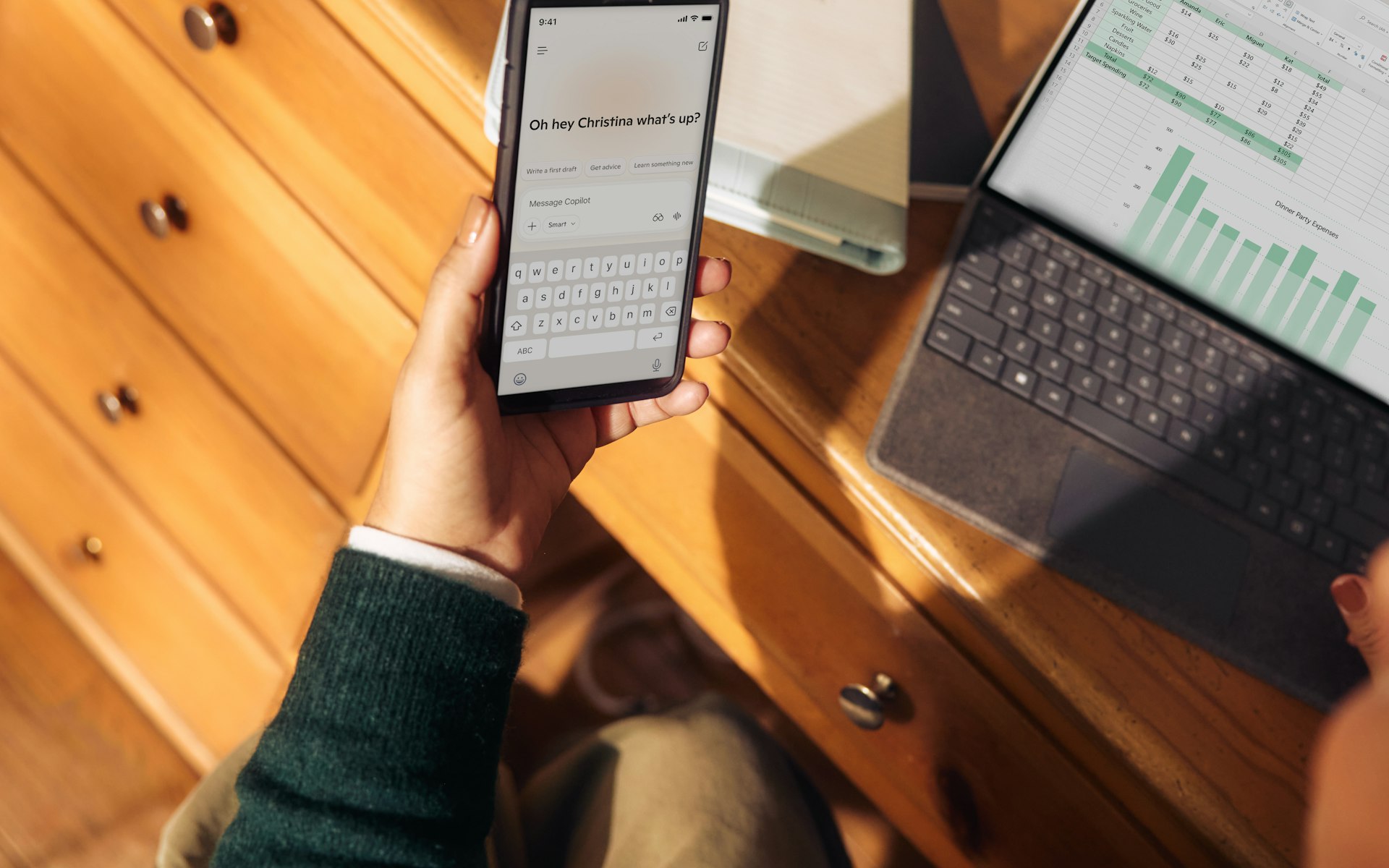 Person holding phone near laptop and tablet on desk